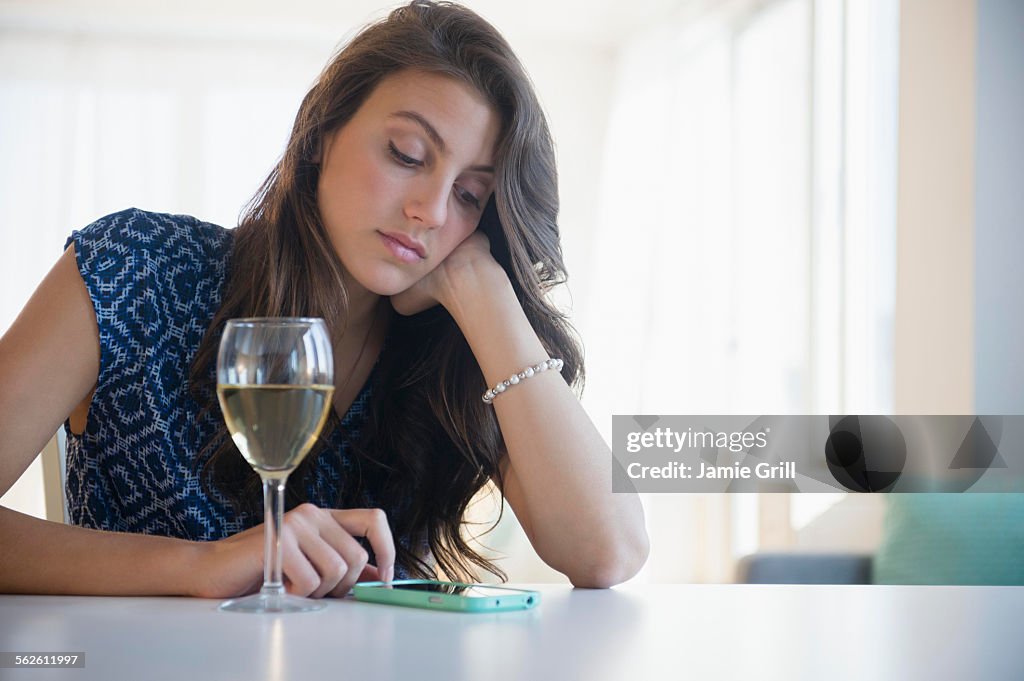 Sad woman with glass of wine texting