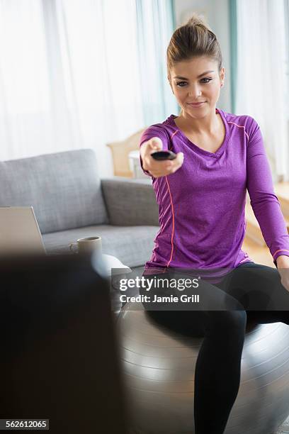 young woman sitting on exercising ball and turning on tv - one woman only videos stock pictures, royalty-free photos & images