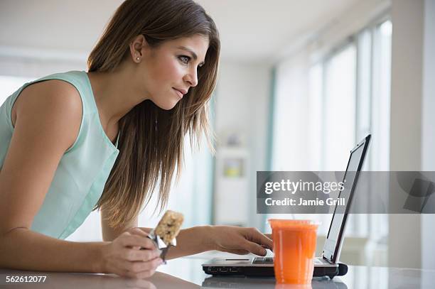 young woman eating snack while working with laptop - snacking on the go stock pictures, royalty-free photos & images