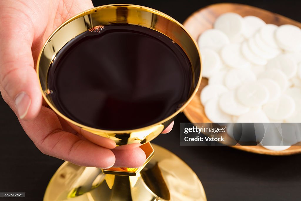 Christian holy communion, mans hand holding gold chalice with wine, communion wafer on plate