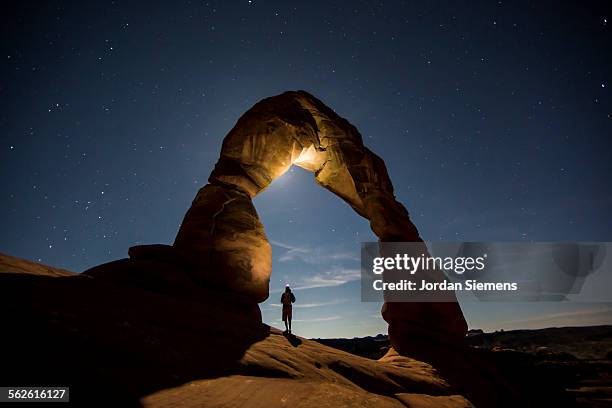 a hiker standing underneath an arch. - delicate arch stock-fotos und bilder