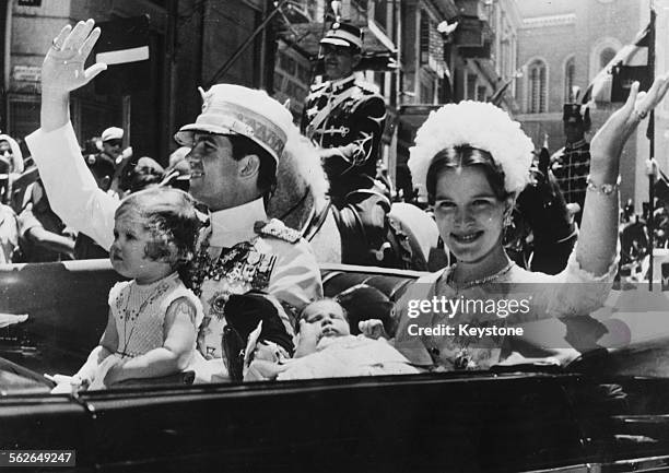 King Constantine of Greece with his wife Anne-Marie and their children, Princess Alexia and Crown Prince Paul, waving to the crowds as they drive...