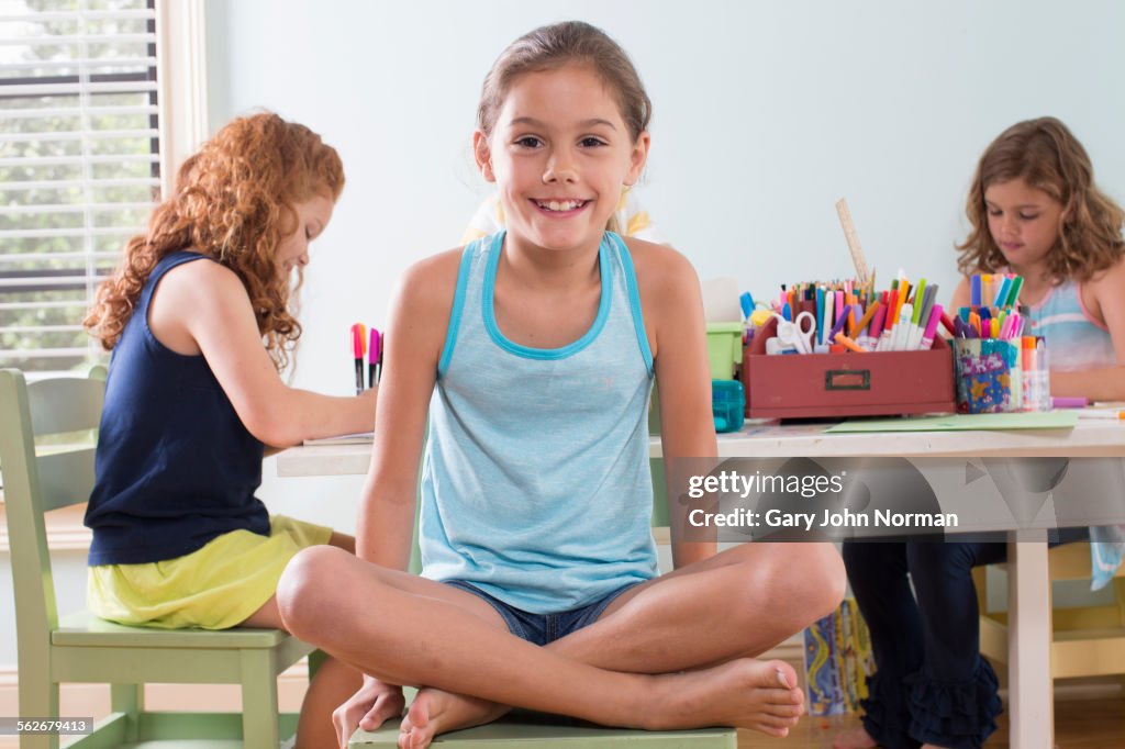 Happy young girl sits cross legged on chair.