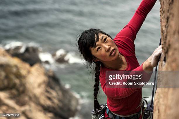 woman climbing up cliff with ocean in background - alpinismo fotografías e imágenes de stock