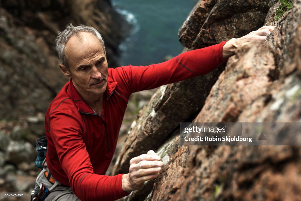 Mature grey haired Man climbing up cliff