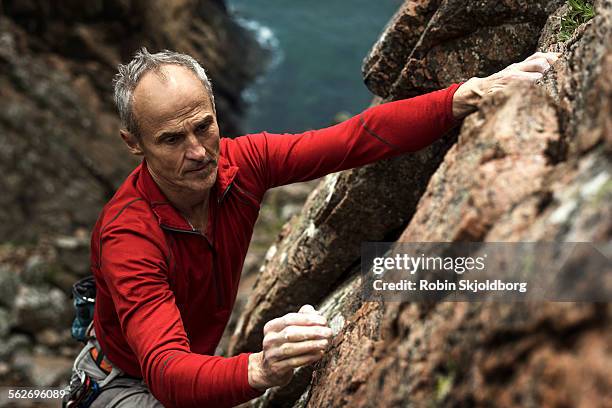 mature grey haired man climbing up cliff - solo un uomo anziano foto e immagini stock