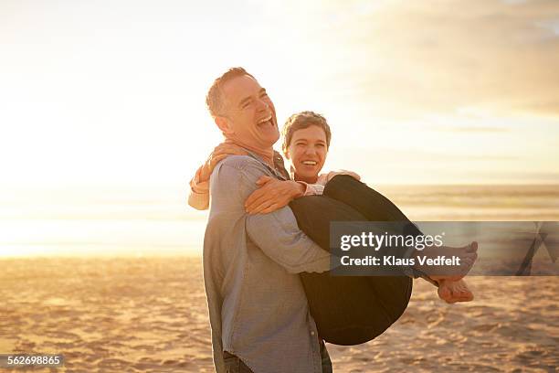 mature man carrying girlfriend on the beach - romantic holiday stock-fotos und bilder