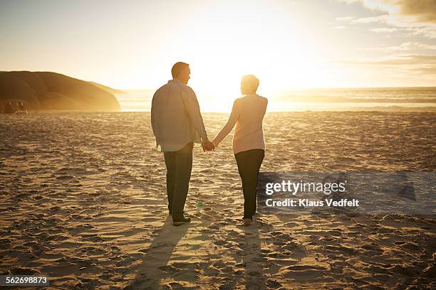 mature couple walking hand in hand on beach - sunset silhouette back lit stock pictures, royalty-free photos & images