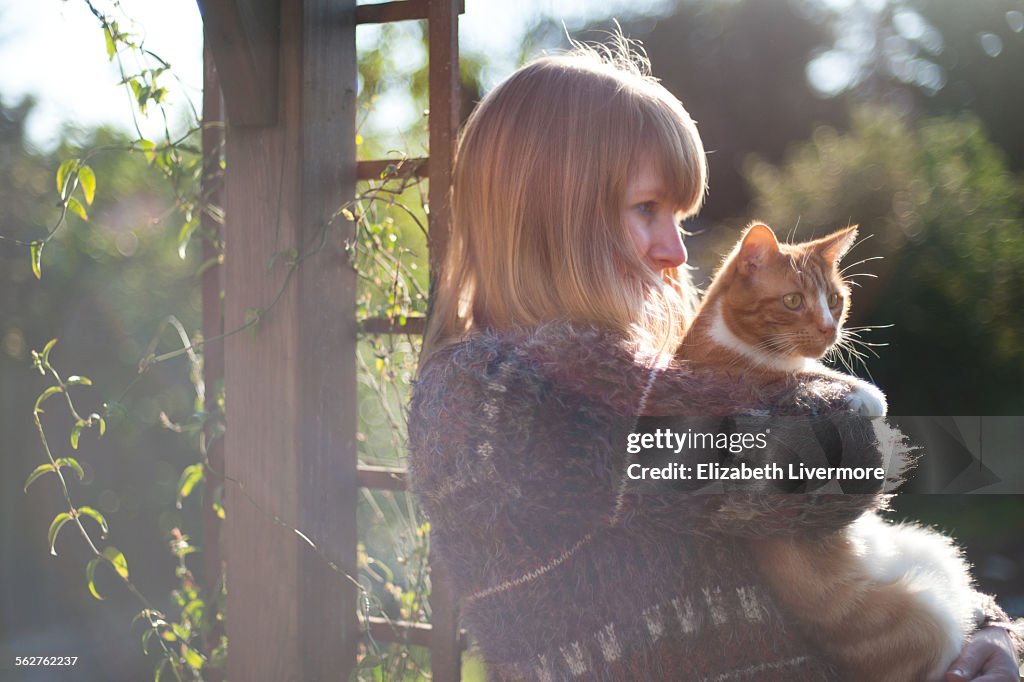 Woman cuddles cat in sunshine
