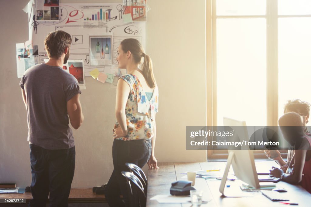 Creative business people reviewing proofs and notes on office wall