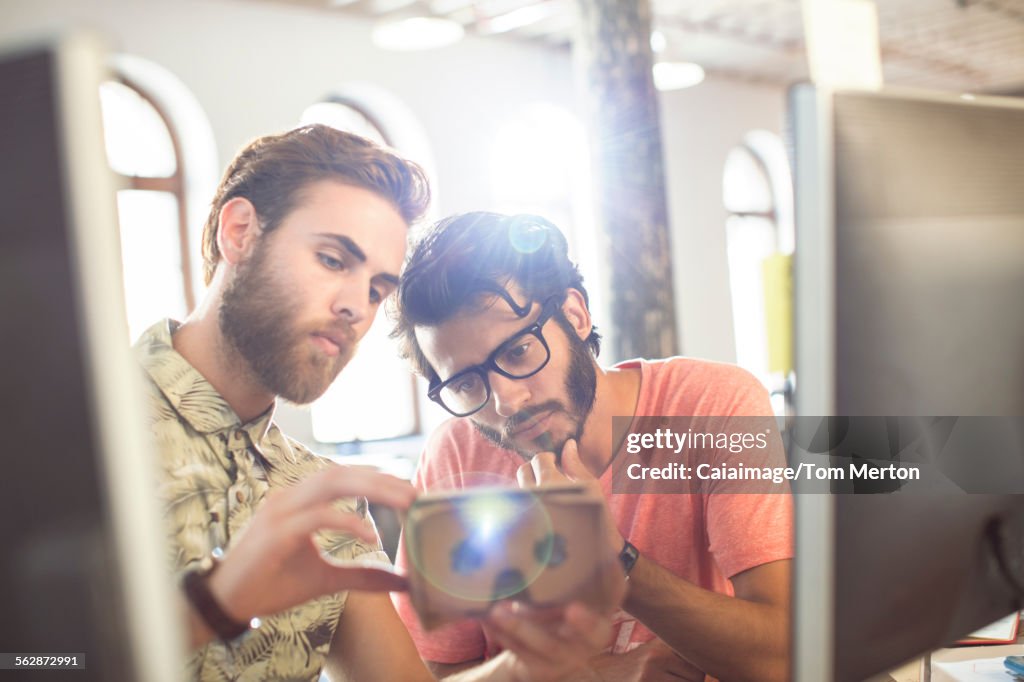 Creative businessmen reviewing proofs at computers in sunny office