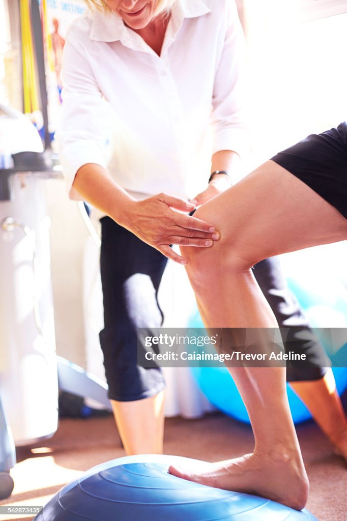 Physical therapist guiding knee of man stepping onto fitness ball