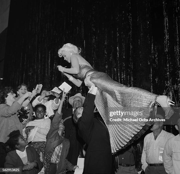 Actress Jayne Mansfield is lifted by Mickey Hargitay as she signs her autograph as they attend the premiere of "Sprit of St Louis" in Los...