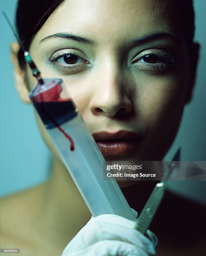 Woman with scalpel and syringe of blood