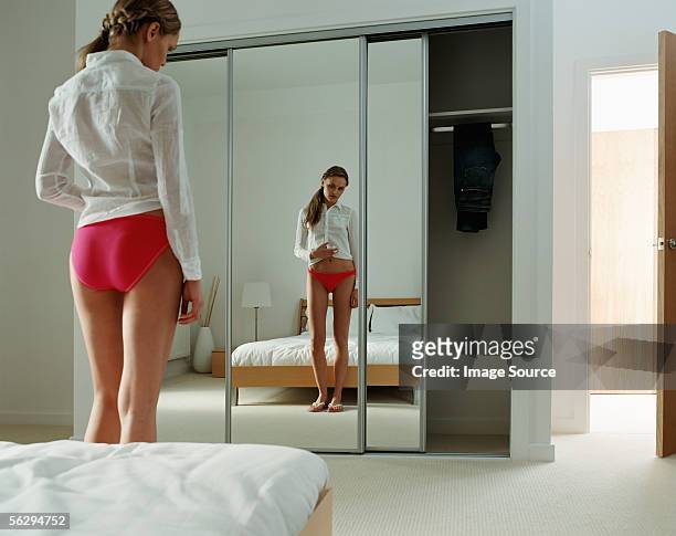 woman looking at her stomach in the mirror - weight gain foto e immagini stock