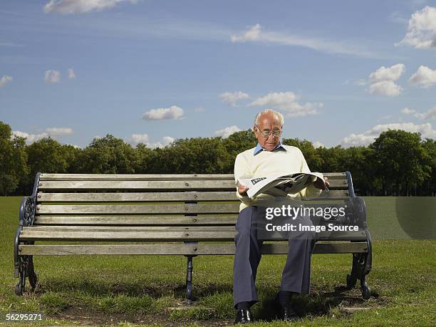 elderly man reading a newspaper in a park - banco del parque fotografías e imágenes de stock