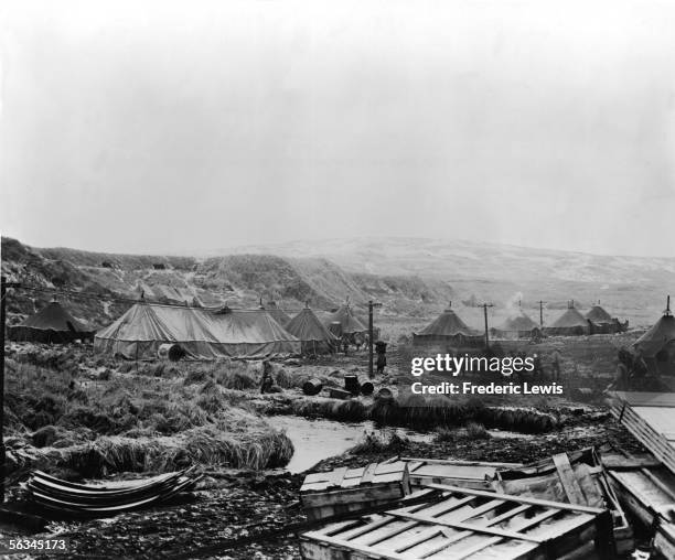 American soldiers trudge through muddy ground near rows of tents in an American army base stationed in the Aleutian Islands, Alaska, December 14,...