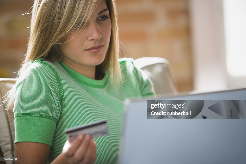 Close-up of a teenage girl holding a credit card sitting in front of a laptop