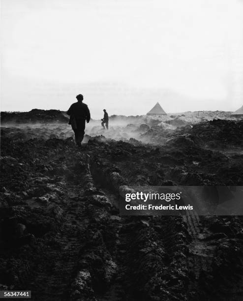 American soldiers trudge through muddy ground near tents of the American base at Attu in the Aleutian Islands, Alaska, July 29, 1943. Tire tracks and...