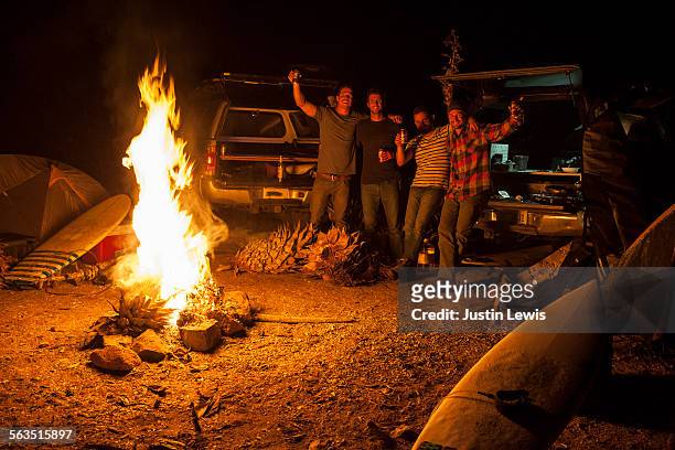 four surfers drink beer by campfire - camp fire stock pictures, royalty-free photos & images