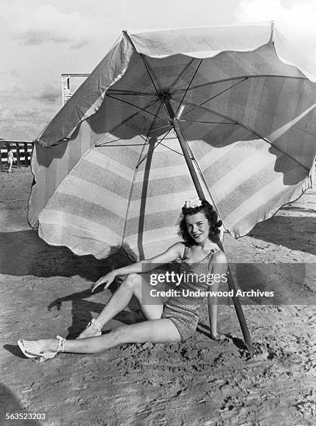 Exotic dancer Thelma Ray Nicholas relaxes under an umbrella on the Galveston beach, Galveston, Texas, circa 1933.