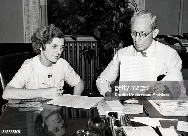 Herbert Hangstler and his assistant Madge Blessing, the US State Department trouble experts of the Foreign Service Division, check over lists of...