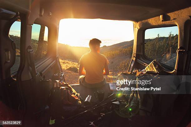 man sitting in car looking at sunset in mountains - man adventure fotografías e imágenes de stock
