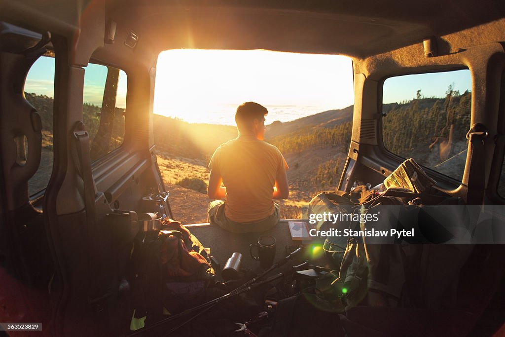 Man sitting in car looking at sunset in mountains