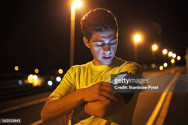 man jogging, checking mobile device at night - virtualitytrend stockfoto's en -beelden
