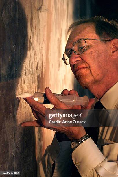 Working curator Perry Huston uses a syringe to inject poly vinyl acetate emulsion into hollow spaces behind the mural entitled "Portrait of Mexico...