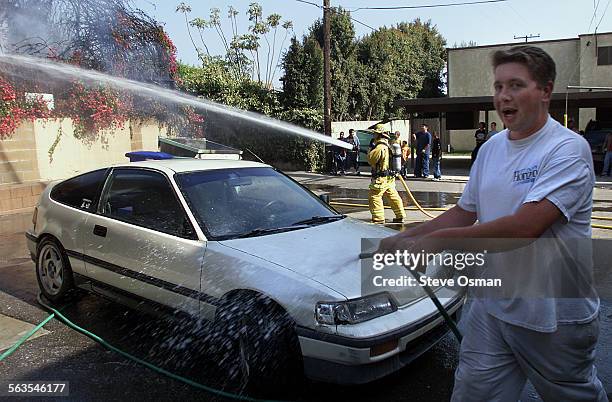 Jason Jefry 26, of Ventura, washes off his Honda CRX, as Ventura City and Ventura County firefighters extinguish a two alarm fire behind a home on...