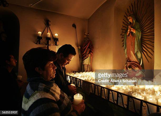 Jorge Merida, far left, Manuel Cortes and wife Ofelia Merida, middle, pray and light candles to honor the Virgin de Guadalupe, whos statue is at...