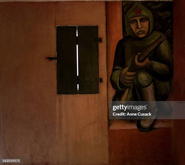 Adjacent to a window with a wooden shutter that is part of the existing structure, is an image of a Communist soldier, kneeling with his rifle. A...