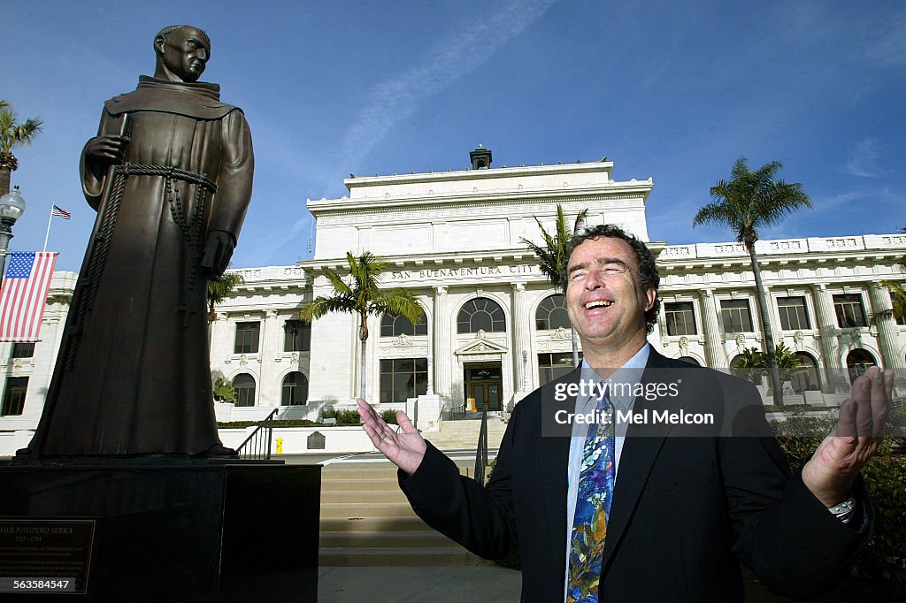 Brian Brennan, mayor of Ventura stands next to statue of Father Junipero Serra, with Ventura City Ha