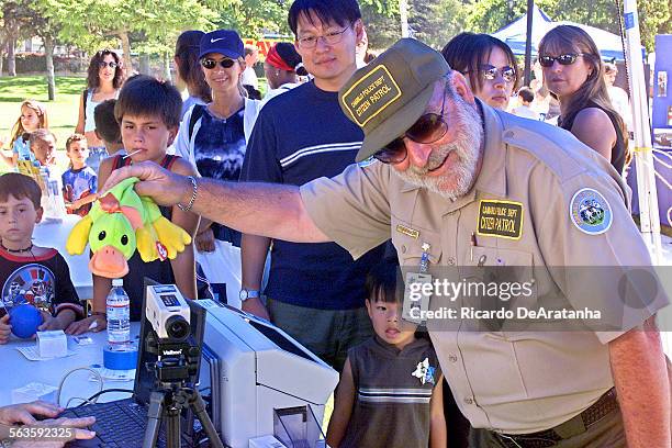 Camarillo Citizen Patrol volunteer David Fish shaking a stuffed animal to attract the attention of a child whose picture is being taken for a new...