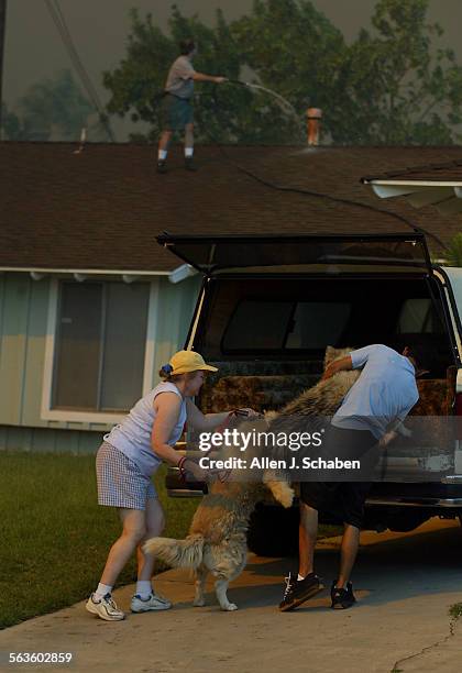 Bob Thibodeau waters down his roof with a garden hose and watches the approaching fire as his wife, Diane and son, Chris evacuate their dogs as Santa...