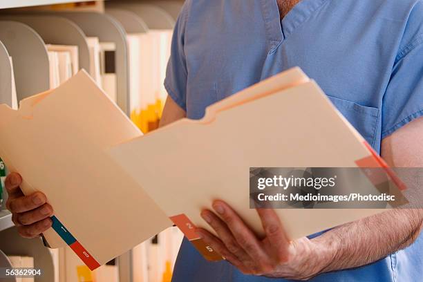 mid section view of a doctor holding medical reports in a medical records room - krankenakte stock-fotos und bilder