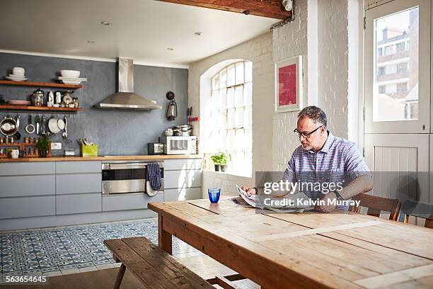 a man sits reading a newspaper at a dining table - table stock pictures, royalty-free photos & images