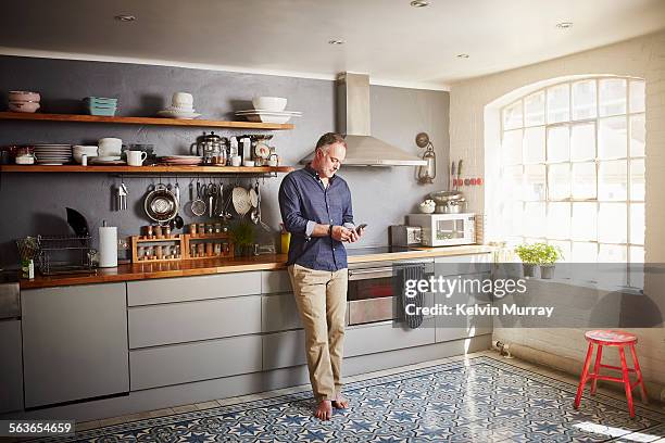 a man stands in his kitchen using a mobile phone - standing at attention stock pictures, royalty-free photos & images