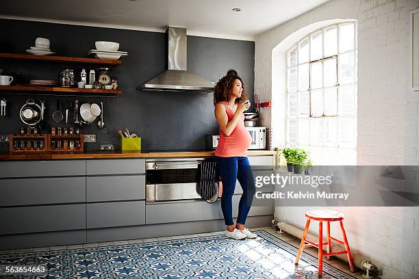 a pregnant lady looks out of her kitchen window - happy moment woman stock-fotos und bilder