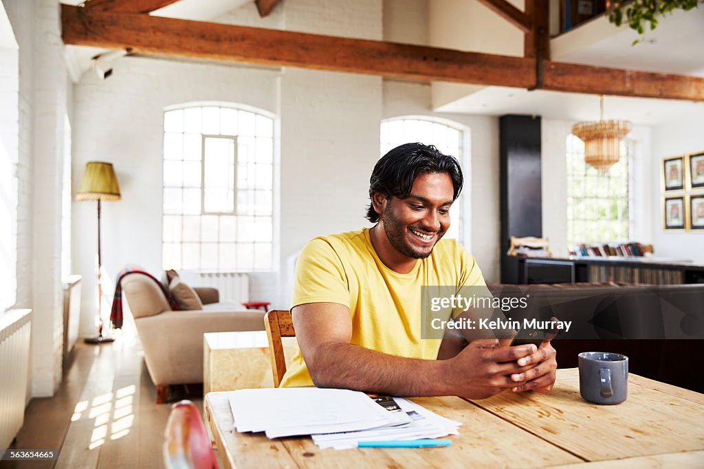 A man smiles whilst using his phone at home