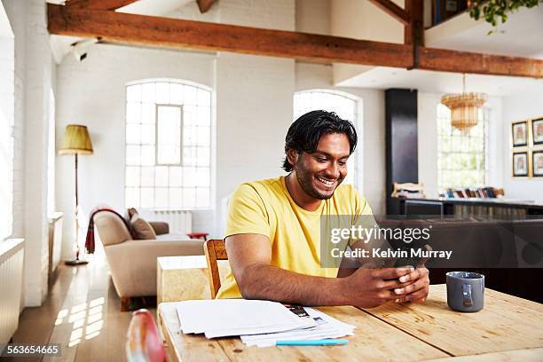 a man smiles whilst using his phone at home - man holding paper stock pictures, royalty-free photos & images