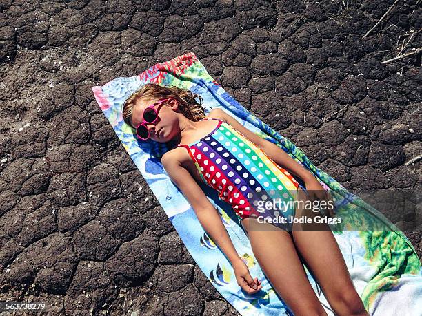 child sun baking on towel on dry parched ground - young girl swimsuit stockfoto's en -beelden