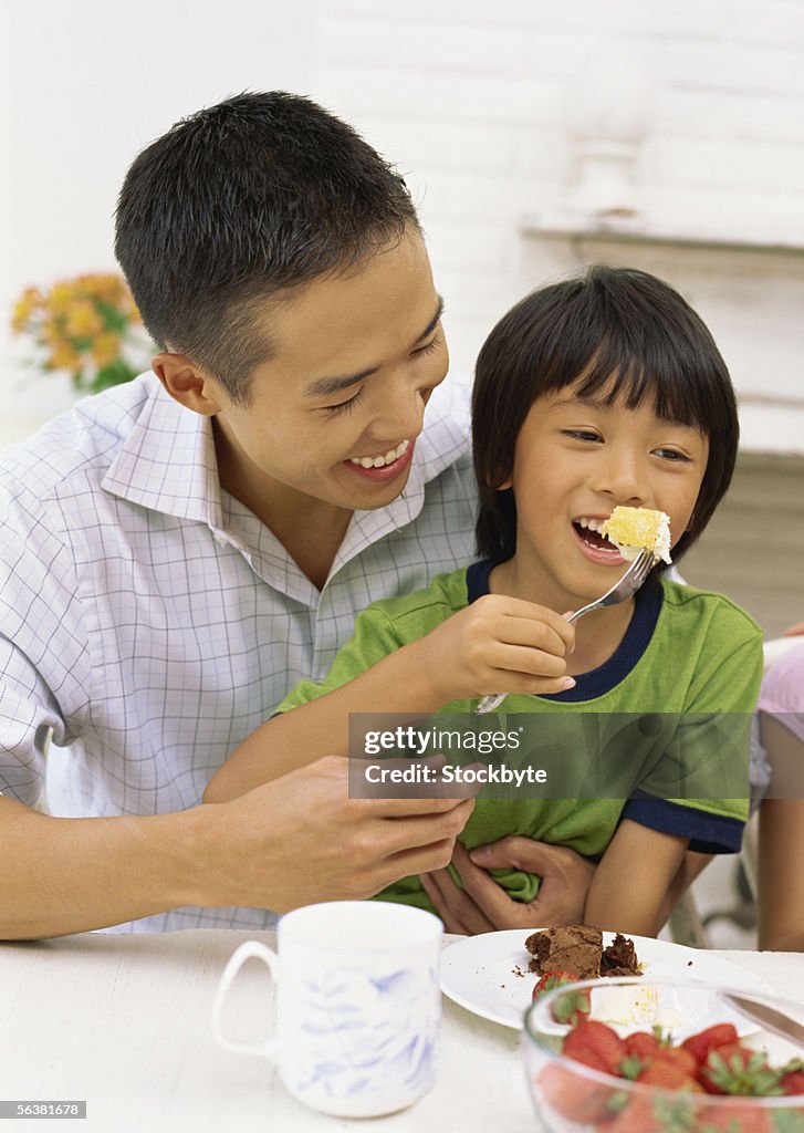 Son sitting with his father eating a piece of cake