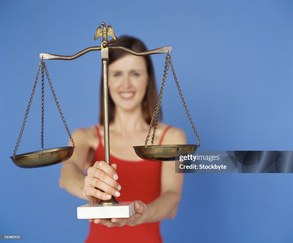 Portrait of a young woman holding a brass weighing scale