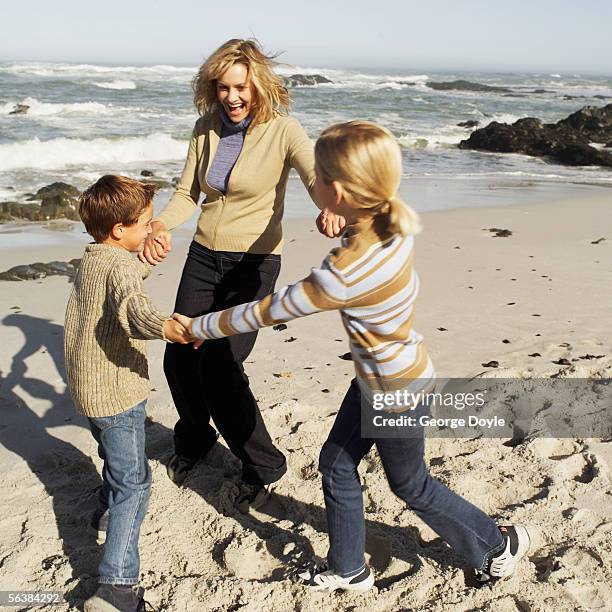 mother with her son and daughter playing ring-around-a-rosy on the beach - ring around the rosy stock pictures, royalty-free photos & images