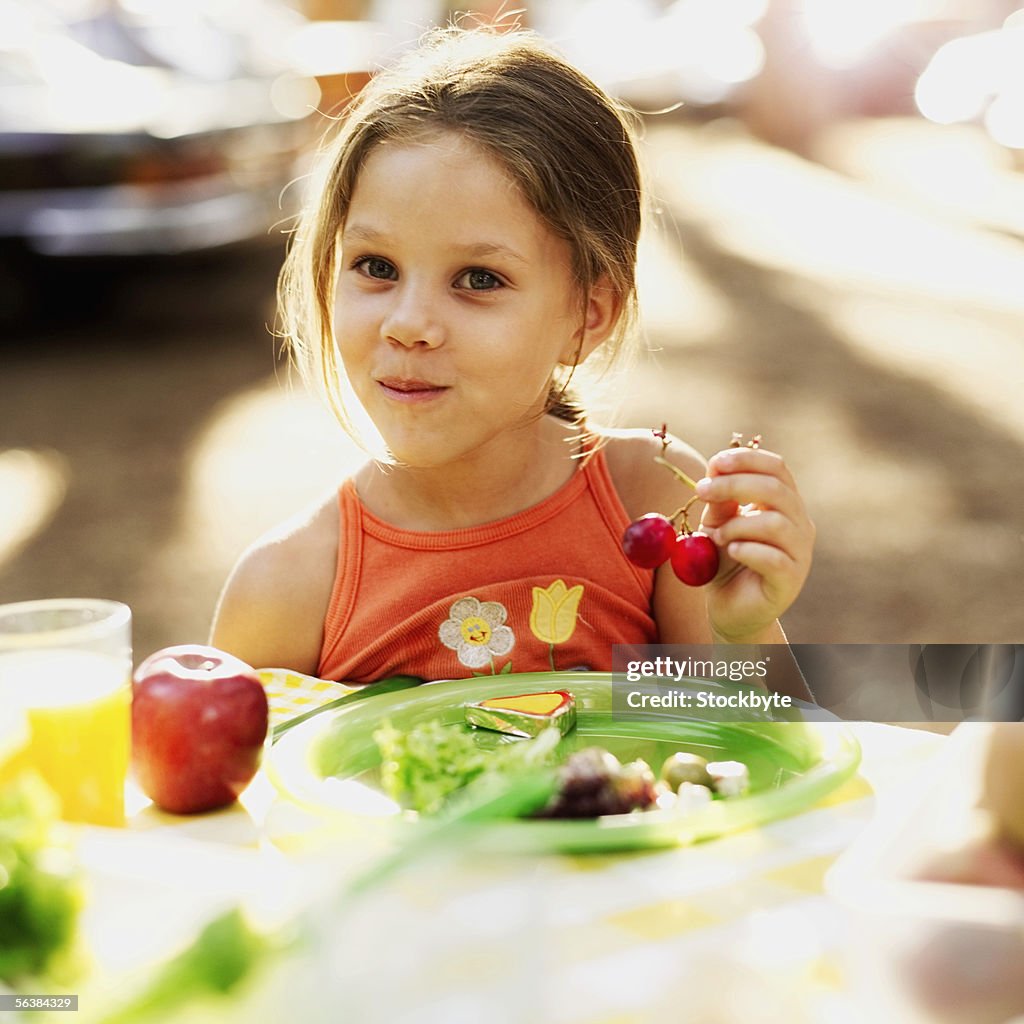 Portrait of a girl sitting at a picnic table holding cherries