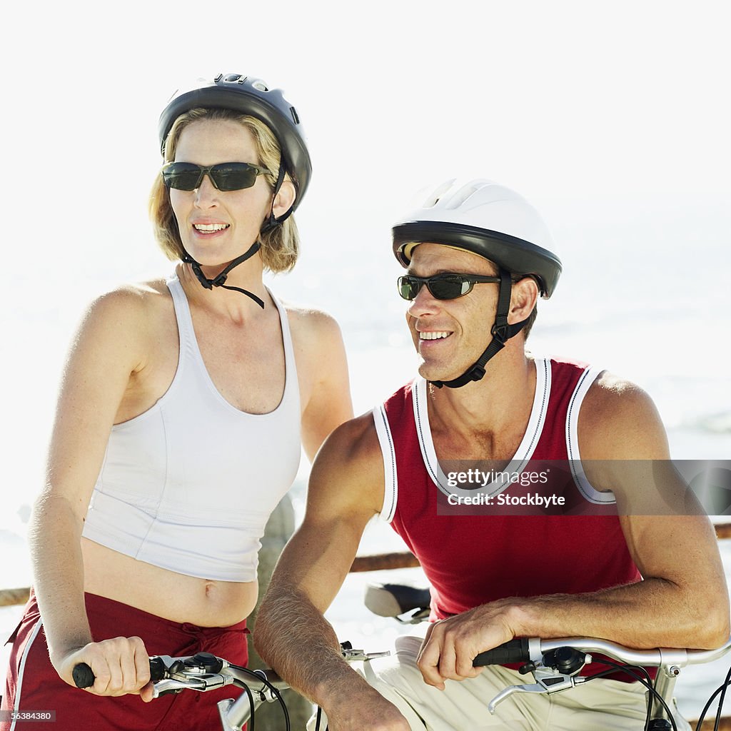 Young couple standing with bicycles wearing cycling helmets and sunglasses