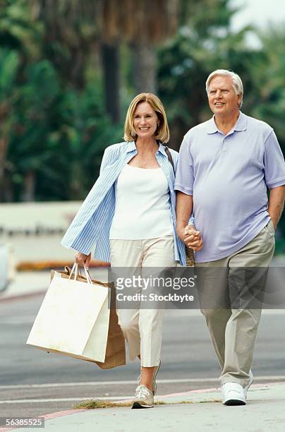 senior couple holding shopping bags - hand in hand spazieren stock-fotos und bilder
