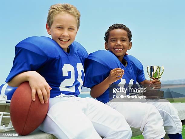 portrait of two boys sitting with a football and a trophy - joueur-de-football-américain photos et images de collection